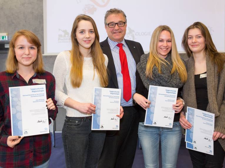 Vier Realschülerinnen stehen jeweils zu zweit rechts und links neben einem Mann im Anzug und halten alle ihre Urkunde in den Händen.